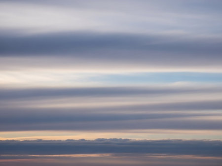 Layered horizontal clouds in muted blues grays and soft peach tones dominate the sky with a sliver of bright blue visible.の素材