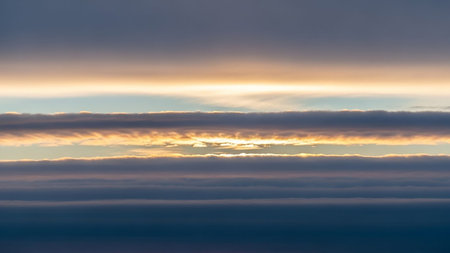 Muted showing horizontal layers of dark grey and muted purple clouds with a bright band of golden sunlight breaking through the middle keywords: sky, clouds,...の素材