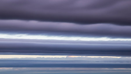 Across showing horizontal layers of dark purple and gray clouds stretch across the frame with thin bands of pale light visible between them creating a dramatic and...の素材