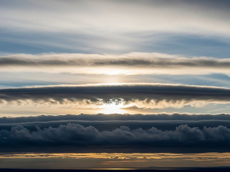 Multiple distinct layers of clouds are illuminated by the setting sun, creating a visually striking banded effect across the sky with warm golden light.の素材