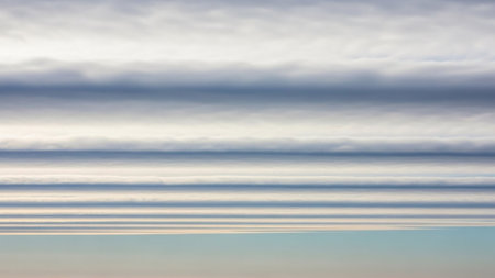 Horizontal layers of undulating grey and white clouds create a striped pattern against a pale blue sky, forming a unique atmospheric texture.の素材