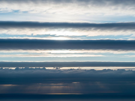 Rays showing horizontal layers of dark and light clouds with sunlight breaking through, casting rays onto a calm body of water below keywords: clouds, sky, water,...の素材