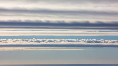 Distinct horizontal layers of white and grey clouds form a striped pattern above a calm blue ocean and a clear sky.の素材
