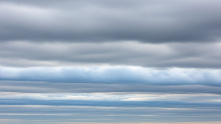 Horizontal bands of gray and pale blue clouds fill the frame, creating a layered, textured sky with subtle shifts in light and shadow.の素材