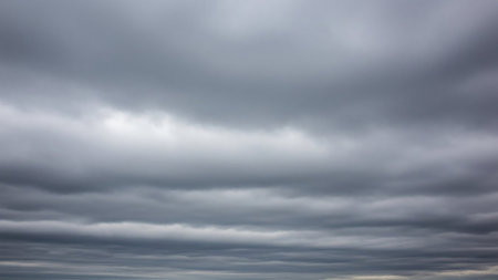 An overcast sky filled with dense, horizontal layers of dark gray cumulus clouds creates a moody and somber atmospheric effect.の素材