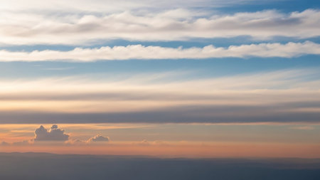 Warm showing horizontal layers of white and blue clouds at sunset with a warm orange glow illuminating the distant horizon and landmass keywords: sky, clouds,...の素材