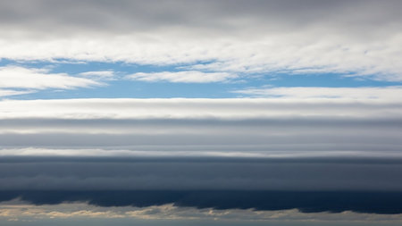 A layered sky distinct horizontal bands of white cirrus clouds, dark grey storm clouds, and bright blue sky, creating a dramatic atmospheric vista.の素材