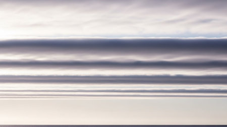 Horizontal bands of grey and white clouds create a layered effect against a pale sky, with a dark horizon line below.の素材
