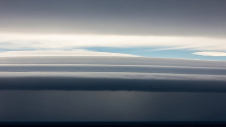 Stock showing layered lenticular clouds forming distinct horizontal bands of white and dark gray against a clear blue sky with subtle sunlight and a dark horizon...の素材