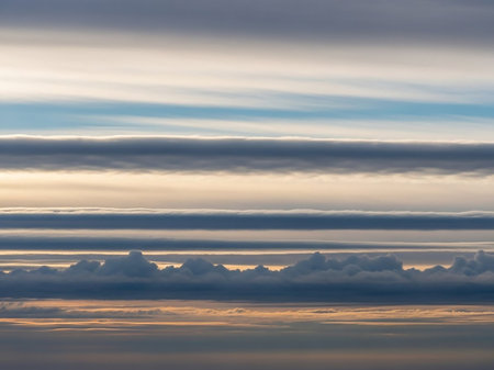 Horizontal layers of diverse cloud formations and sky colors create a textured atmospheric landscape with soft golden light.の素材