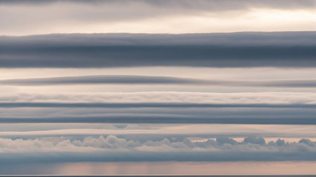 Distinct horizontal layers of gray and soft pink clouds create a dramatic, abstract pattern against a subtle ocean horizon.の素材
