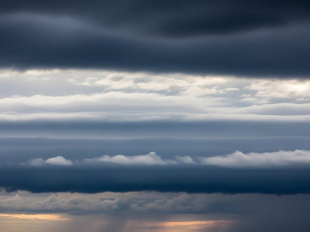 Form showing layered dark and light grey clouds form distinct horizontal bands across the sky with faint sunlight and rain shafts below keywords: clouds, sky,...の素材