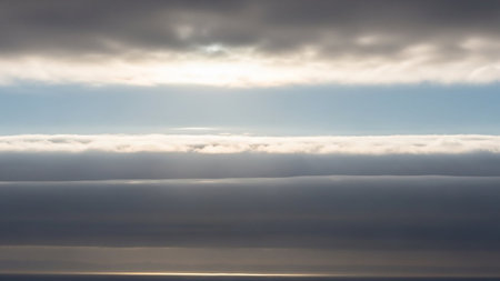 Horizontal layers of clouds and sunlight create a striking skyscape above a sunlit ocean horizon, with a bright band of light.の素材