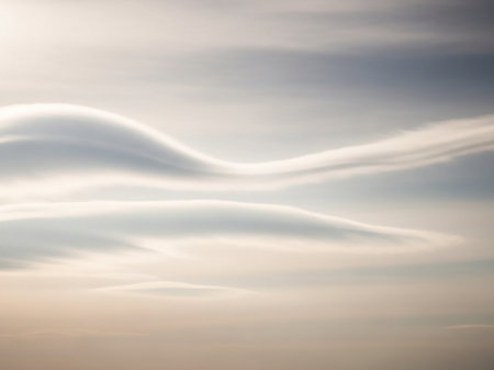 Unusual showing lenticular clouds forming unusual wave-like shapes in a softly lit sky with subtle hues of blue and peach creating a surreal landscape.の素材