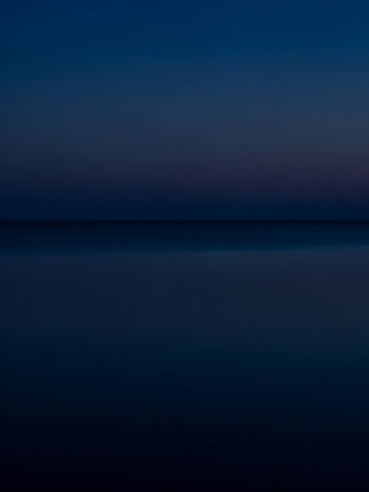 Twilight showing minimalist dark blue horizon line dividing the deep blue sky and the calm dark ocean at twilight with a serene and tranquil atmosphere.の素材