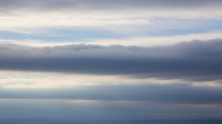 Horizontal layers of dark grey and lighter grey clouds dominate the frame, with streaks of bright white light and hints of pale blue sky visible between them.の素材