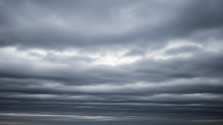 A vast expanse of sky is filled with horizontal layers of dark gray stratus clouds, creating a moody and somber atmosphere.の素材