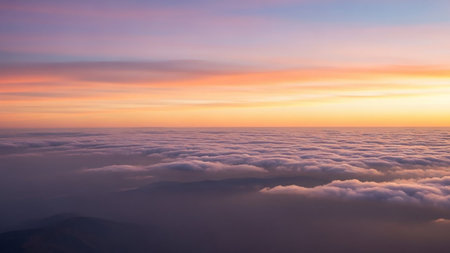 An aerial view above a blanket of soft clouds at sunset, with a gradient sky of orange, pink, and purple hues.の素材