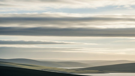 Stock showing rolling hills and valleys under a softly lit sky with horizontal cloud layers and a distant body of water. resolutionの素材