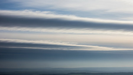 Meteorological showing overlooking rolling hills and distant landscape under a sky filled with horizontal grey and white stratocumulus clouds keywords: clouds, sky,...の素材