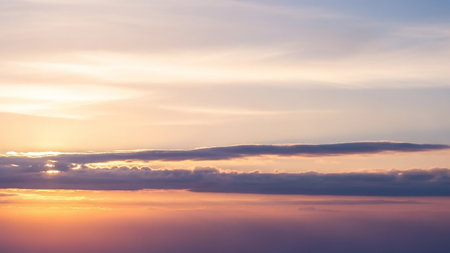 A tranquil sky at sunset soft orange, pink, and blue hues with wispy clouds and golden light breaking through.の素材