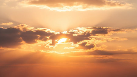 Golden hour sunset with bright sunbeams piercing through dark, dramatic clouds, casting warm orange and yellow light across the sky.の素材