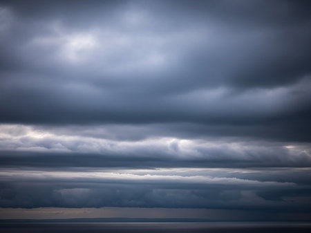 An overcast sky filled with heavy dark gray clouds and a thin bright horizon line above a calm water surface.の素材