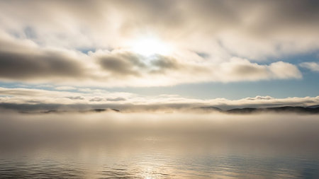 A misty, tranquil scene over water with silhouetted hills in the distance and sunlight piercing through clouds.の素材