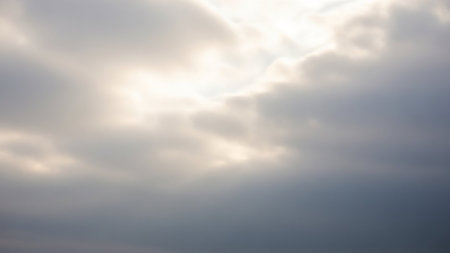 Soft, diffused sunlight filters through a hazy, overcast sky with gentle cloud formations, creating a muted and serene atmospheric background.の素材