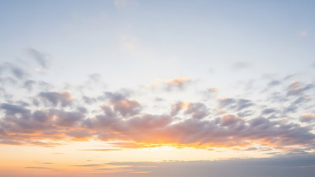 A soft pastel sky at sunrise wispy clouds with a gentle glow of orange and yellow light on the horizon.の素材