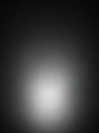 A dark gray textured surface illuminated by a bright white light source at the bottom center, creating a soft gradient and diffused glow effect.の素材