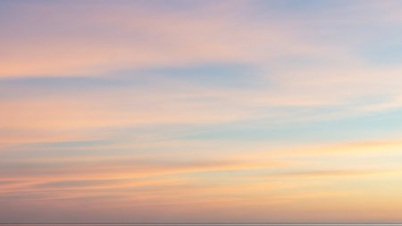 Gentle showing soft pastel colored sky with horizontal streaks of pink, peach, blue, and yellow creating a serene and tranquil atmospheric background at dawn or...の素材