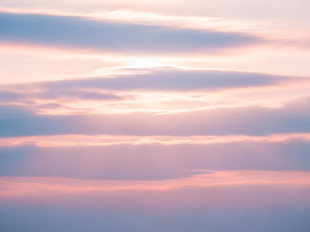 Horizontal layers of soft pink and blue clouds are illuminated by diffused sunlight, creating a tranquil and dreamy atmospheric sky.の素材