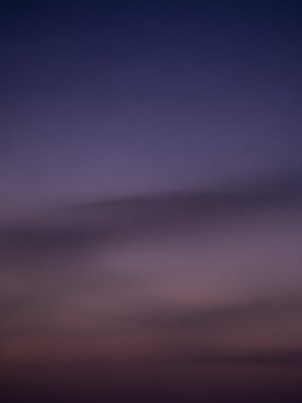 A soft gradient of twilight sky transitions from deep indigo blue to muted lavender and dusky rose, with a hazy atmospheric effect.の素材