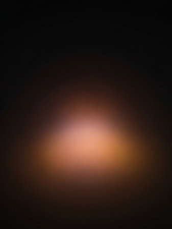 Gentle showing softly glowing warm orange and pink light emanating from a central point against a dark blurred background creating an abstract bokeh effect...の素材