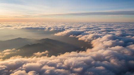 Stock showing aerial view above a sea of golden clouds at sunrise or sunset with silhouetted mountain peaks emerging below the soft light. resolutionの素材