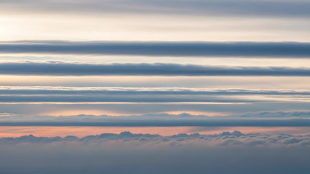 Meteorological showing aerial view of layered stratocumulus clouds at sunrise with soft pastel hues of orange and pink illuminating the sky above a dense cloud...の素材
