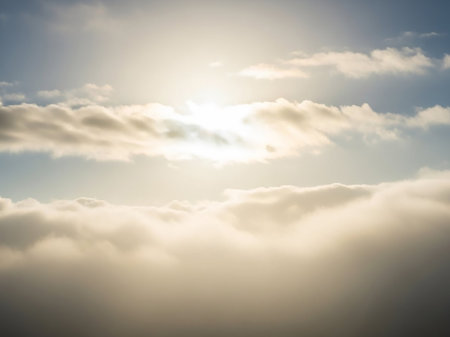 Bright sunlight shines through soft white and golden clouds against a blue sky, creating a luminous atmospheric effect.の素材