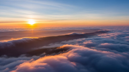 An aerial view captures mountain peaks rising from a sea of soft clouds at sunrise, bathed in warm golden orange sunlight.の素材