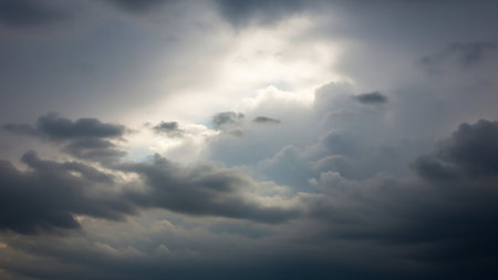 Dramatic dark grey storm clouds with bright white light breaking through the center, creating a powerful, dynamic contrast in the sky.の素材