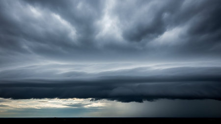 Dark, layered storm clouds fill the sky, with a distinct band of rain falling on the distant horizon under a pale, overcast light.の素材