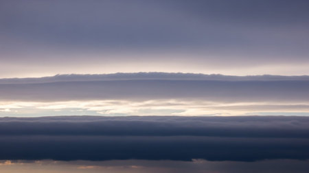 Stock showing horizontal layers of wispy stratocumulus clouds illuminated by soft sunlight creating a serene and atmospheric sky scene with gradient tones of grey...の素材