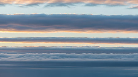 Horizontal showing layered horizontal clouds in shades of grey blue and soft orange at sunrise or sunset creating a dramatic and textured atmospheric vista...の素材
