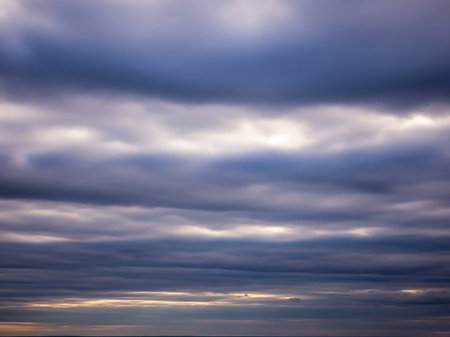 Stock showing overcast sky with layers of dark gray and purple clouds partially lit by faint golden sunlight near the horizon. resolutionの素材