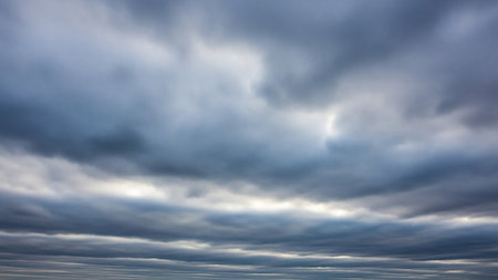 A sky filled with dense, layered grey and dark blue storm clouds creates a dramatic and moody atmosphere, with subtle light breaking through.の素材