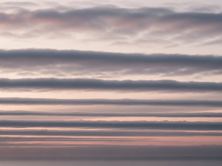 Stratus showing layered stratus clouds in muted pink and gray tones forming horizontal bands over a calm sea at sunset. resolutionの素材