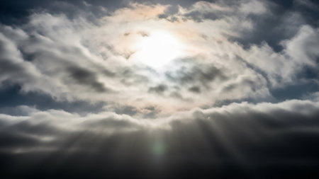 Bright sunlight pierces through dark, swirling storm clouds, casting visible rays of light downwards in a powerful atmospheric display.の素材