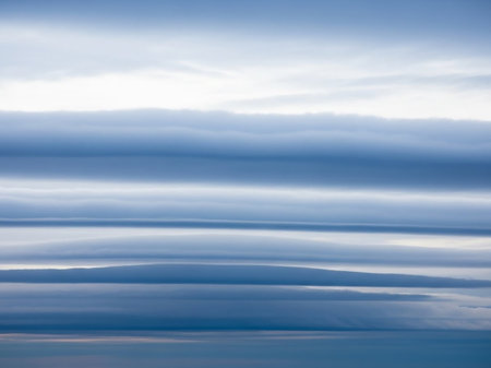 Horizontal layers of wispy, undulating clouds in pale blue and white create a serene, abstract atmospheric landscape with a sense of vastness.の素材