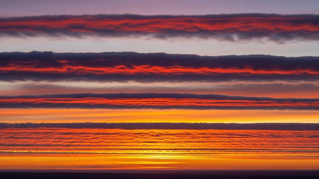 Purple showing striking horizontal cloud formations painted with vibrant fiery red orange and deep purple hues during a dramatic sunset creating a layered...の素材