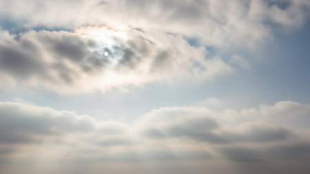 The sun is partially hidden by thick grey clouds, casting soft light rays and revealing a bright sun disc.の素材